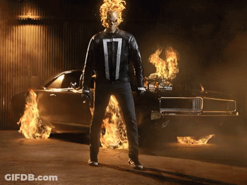 A Ghost Rider Standing In Front Of A Burning Car GIF