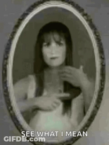 A Ghostly Woman Is Pointing At Herself In A Mirror . GIF