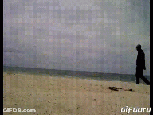 A Gif Of A Man Standing On A Sandy Beach With The Words Gif Guru Below Him GIF