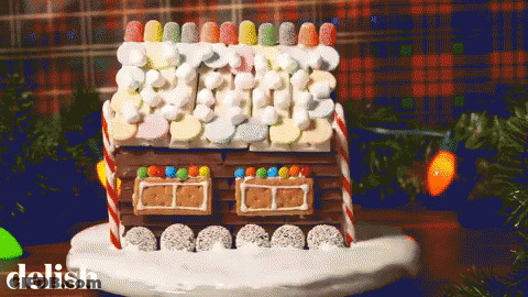 A Gingerbread House Decorated With Marshmallows And Candy Canes On A Plate With The Word Delish Below It GIF