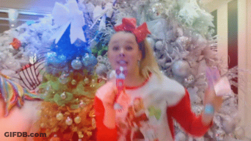 A Girl Blowing Bubbles In Front Of Christmas Trees GIF