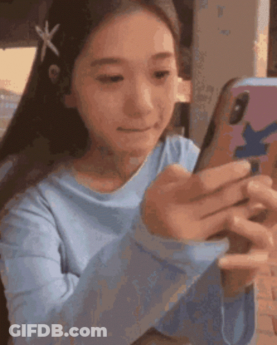 A Girl In A Blue Shirt Is Looking At A Cell Phone . GIF
