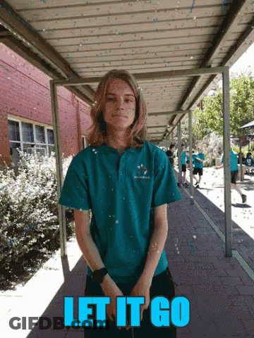 A Girl In A Blue Shirt Stands Under A Covered Walkway With The Words Let It Go GIF