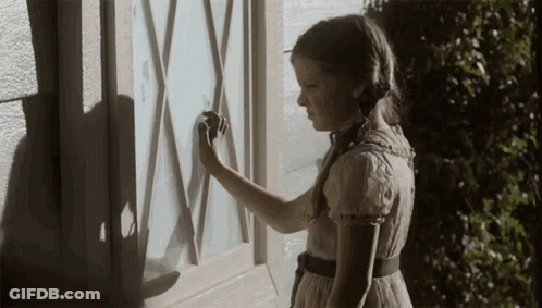 A Girl In A Dress Is Standing In Front Of A Window With A Shadow On It GIF