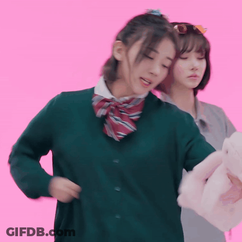 A Girl In A Green Sweater Is Standing Next To Another Girl In A Grey Shirt GIF