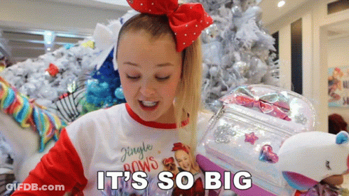 A Girl In A Jingle Bows Shirt Is Holding A Stuffed Unicorn GIF