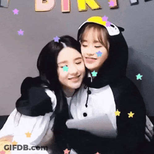 A Girl In A Penguin Costume Is Hugging Another Girl In Front Of A Sign That Says Pink GIF
