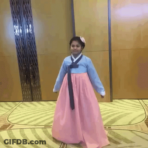 A Girl In A Pink And Blue Dress Is Standing On A Rug GIF