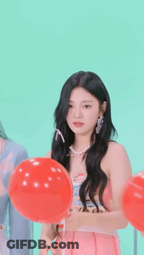 A Girl In A Pink Dress Is Holding A Red Balloon In Front Of Her Face . GIF