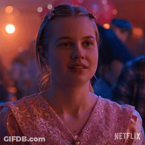A Girl In A Pink Dress Is Sitting In A Room With A Netflix Logo On The Bottom Right Corner . GIF