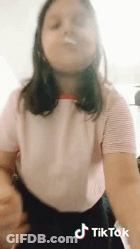 A Girl In A Pink Shirt And Black Skirt Is Making A Tik Tok Video . GIF