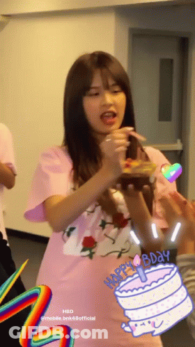 A Girl In A Pink Shirt Is Holding A Birthday Cake With A Candle On It GIF