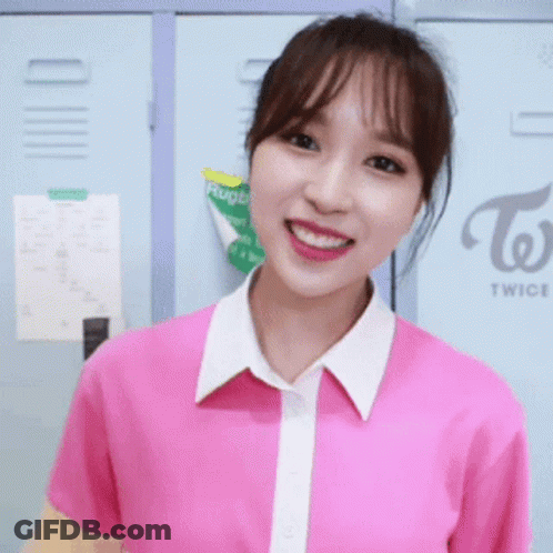A Girl In A Pink Shirt Is Smiling In Front Of A Twice Sign GIF