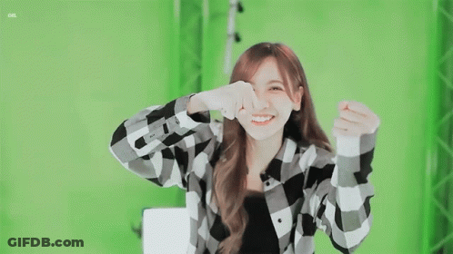 A Girl In A Plaid Shirt Is Smiling And Making A Heart Shape With Her Hands GIF