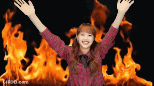 A Girl In A Plaid Shirt Is Standing In Front Of A Large Fire GIF