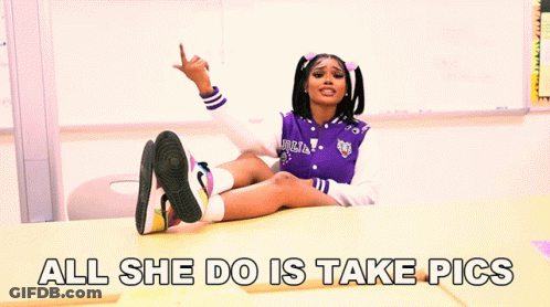 A Girl In A Purple Jacket Sits At A Desk With The Words All She Do Is Take Pics GIF