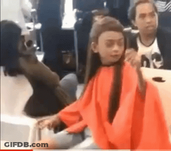 A Girl In A Red Cape Is Sitting At A Table In A Room . GIF