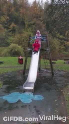 A Girl In A Red Raincoat Is Laying On The Ground In Front Of A Slide In A Park .. GIF