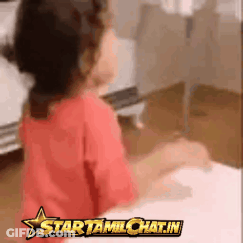 A Girl In A Red Shirt Is Sitting At A Table With A Star Tamilchat.in Logo In The Corner GIF