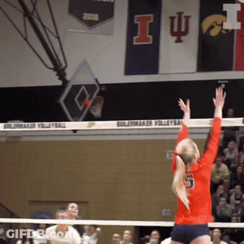 A Girl In A Red Shirt With The Number 5 On The Back Is Jumping Over A Volleyball Net GIF