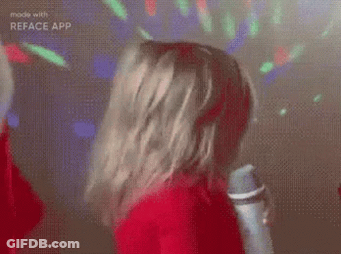 A Girl In A Red Sweater Is Holding A Microphone And Singing . GIF