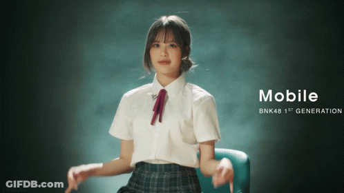 A Girl In A School Uniform Is Sitting In A Chair With The Words Mobile Bnk48 1St Generation On The Bottom GIF