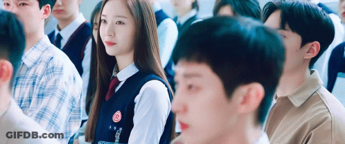 A Girl In A School Uniform Is Sitting In A Classroom With Other People . GIF