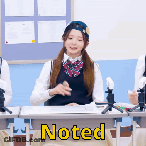 A Girl In A School Uniform Sits At A Desk With The Word Noted On The Front GIF