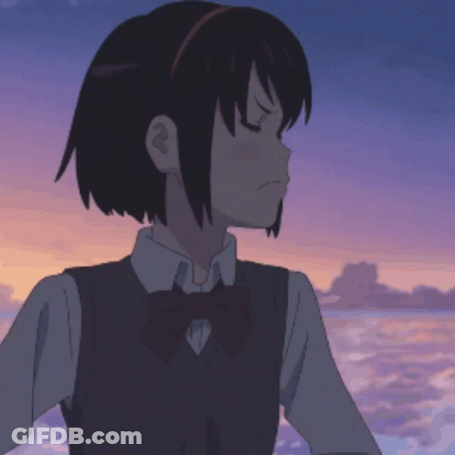 A Girl In A School Uniform With A Bow Tie Is Standing In Front Of The Ocean GIF