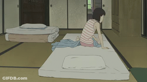 A Girl In A Striped Shirt Sits On A Mattress In A Room GIF