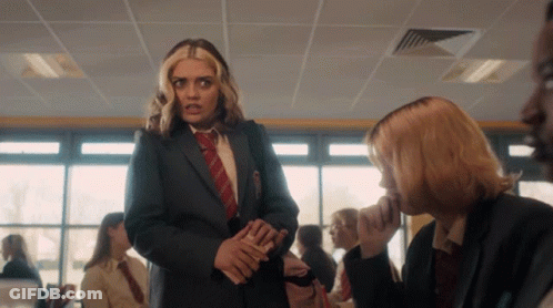 A Girl In A Suit And Tie Talks To Another Girl In A Classroom GIF