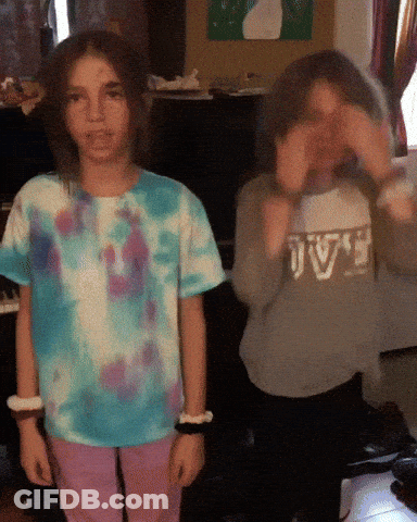 A Girl In A Tie Dye Shirt Is Standing Next To Another Girl Wearing A Sweater That Says Jv GIF