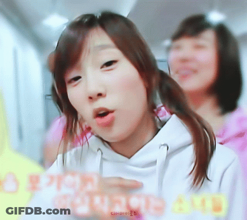 A Girl In A White Hoodie Is Making A Funny Face In Front Of Another Girl GIF