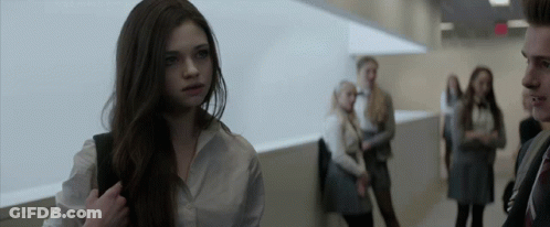 A Girl In A White Shirt Stands In A Hallway With Other People GIF