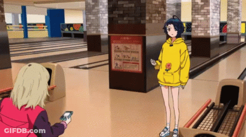 A Girl In A Yellow Hoodie Is Standing In A Bowling Alley While Another Girl Looks At Her Phone . GIF