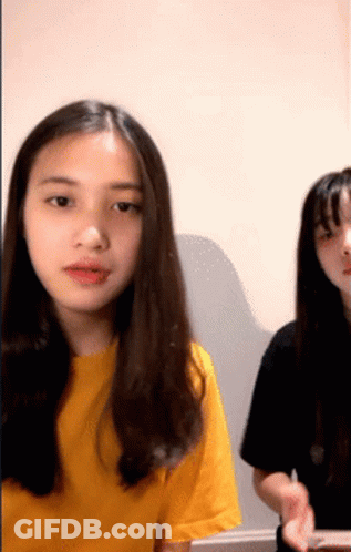 A Girl In A Yellow Shirt Is Sitting Next To Another Girl In A Black Shirt GIF