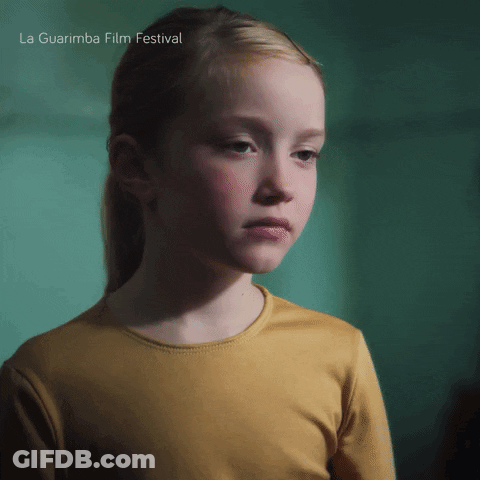A Girl In A Yellow Shirt Is Standing In Front Of A Green Wall And The Words La Guarimba Film Festival Are Above Her GIF