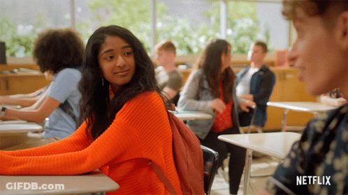 A Girl In An Orange Sweater Sits At A Desk In A Classroom With A Netflix Logo On The Bottom GIF