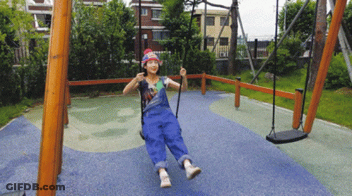 A Girl In Overalls Is Swinging On A Swing Set GIF
