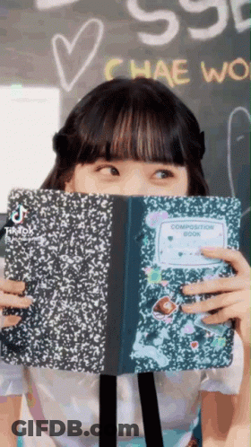 A Girl Is Covering Her Face With A Composition Book GIF