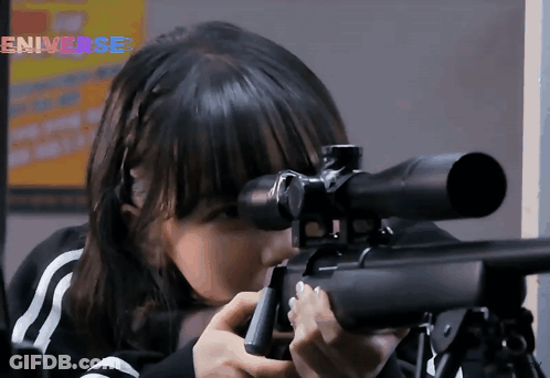 A Girl Is Holding A Sniper Rifle In Front Of An Eniverse Sign GIF