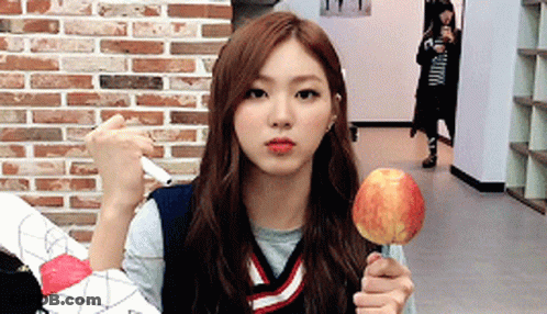 A Girl Is Holding An Apple On A Stick In Front Of A Brick Wall .. GIF