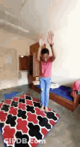 A Girl Is Jumping In The Air In A Room With A Rug . GIF