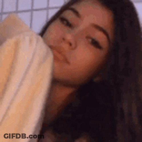 A Girl Is Laying On A Bed With A Towel Around Her Neck . GIF