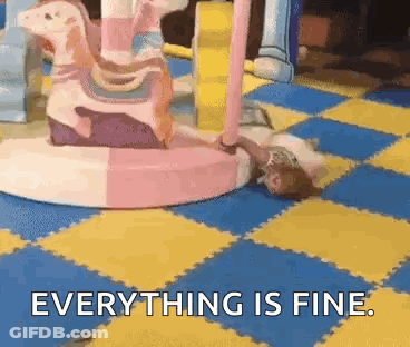 A Girl Is Laying On The Floor In Front Of A Merry Go Round And Says Everything Is Fine . GIF