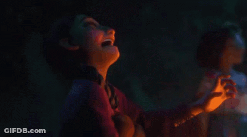 A Girl Is Looking At A Lit Candle In A Dark Room GIF