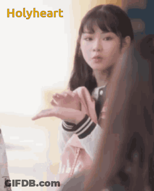 A Girl Is Making A Heart Shape With Her Hands And The Word Holyheart Is Visible Behind Her GIF