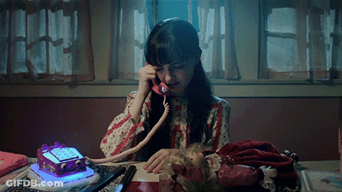 A Girl Is Sitting At A Desk Talking On A Telephone GIF