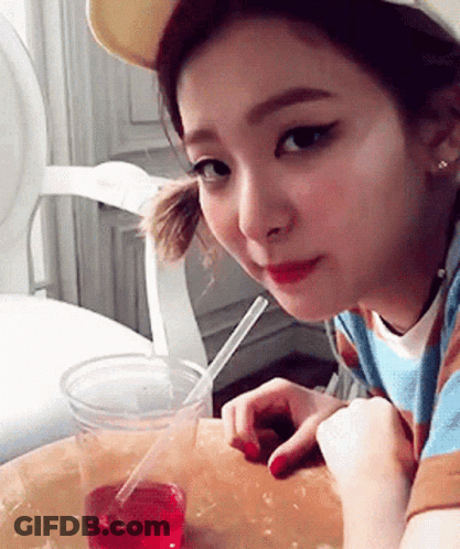 A Girl Is Sitting At A Table With A Cup Of Liquid And A Straw GIF