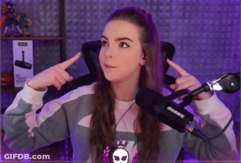A Girl Is Sitting In Front Of A Shure Microphone And Pointing At Herself . GIF